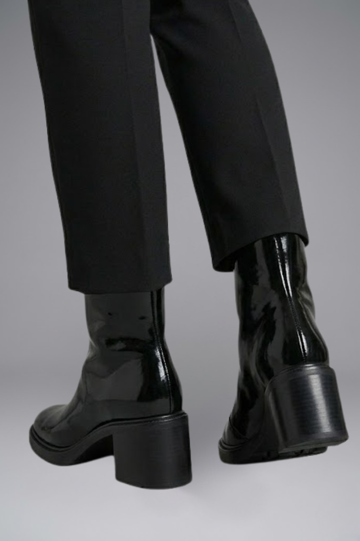 Black patent leather boots worn with black pants on a gray background