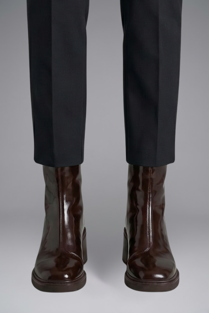Brown leather boots worn with black pants on a gray background