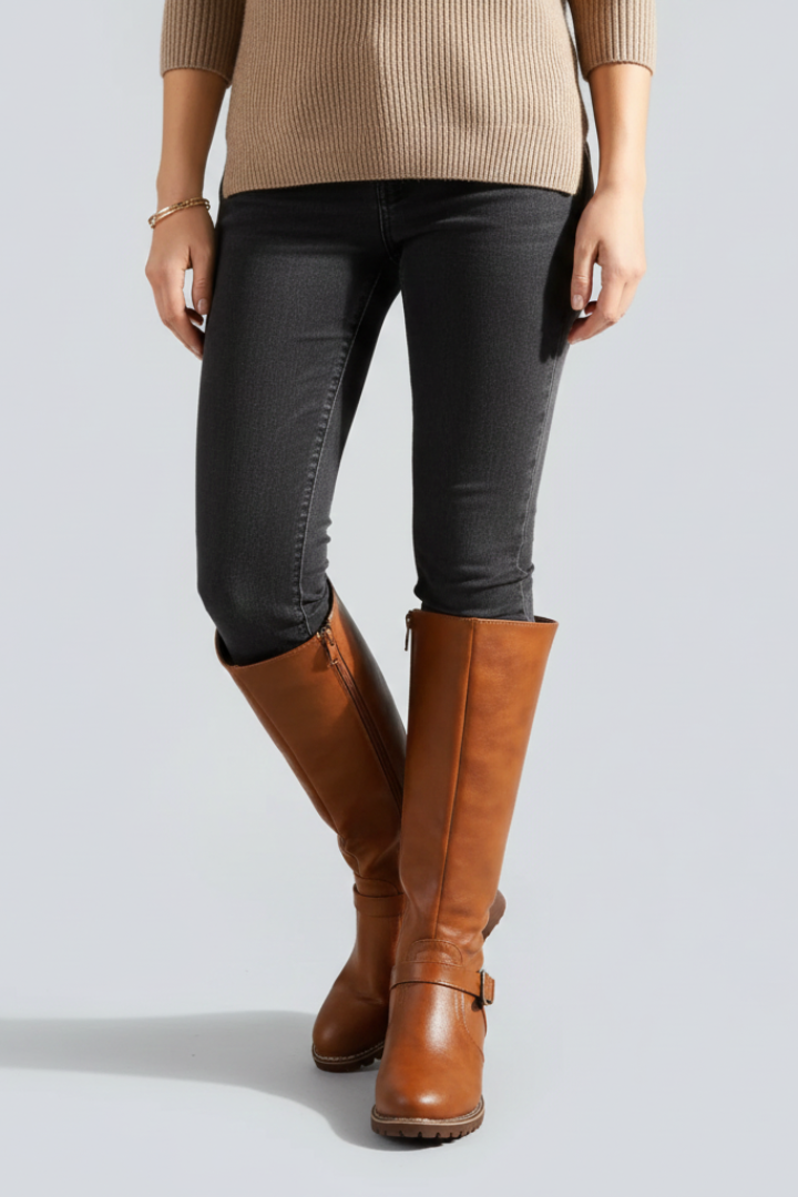 Person wearing brown knee-high boots, black pants, and a beige sweater on a light gray background