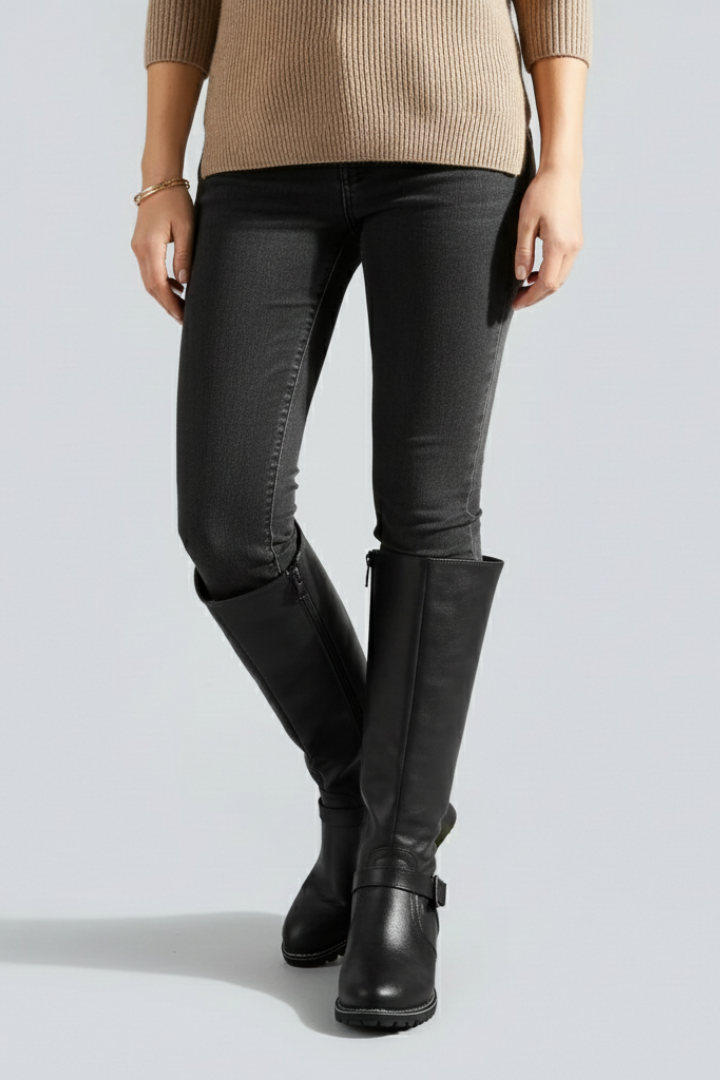 Person wearing black knee-high boots with a plain background