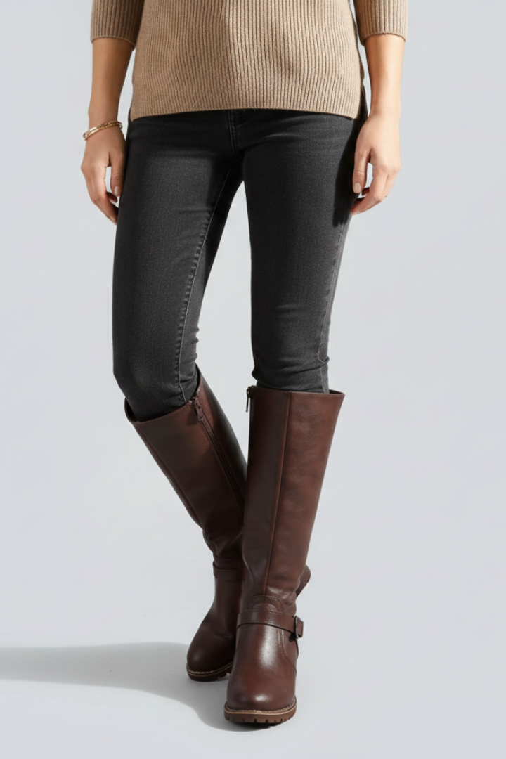 Person wearing brown knee-high boots, black pants, and a beige sweater on a light gray background