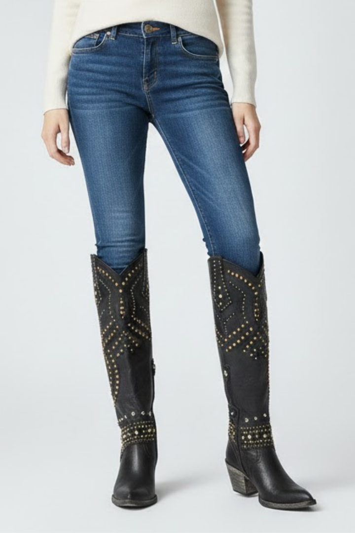 Person wearing blue jeans and black studded knee-high boots on a white background