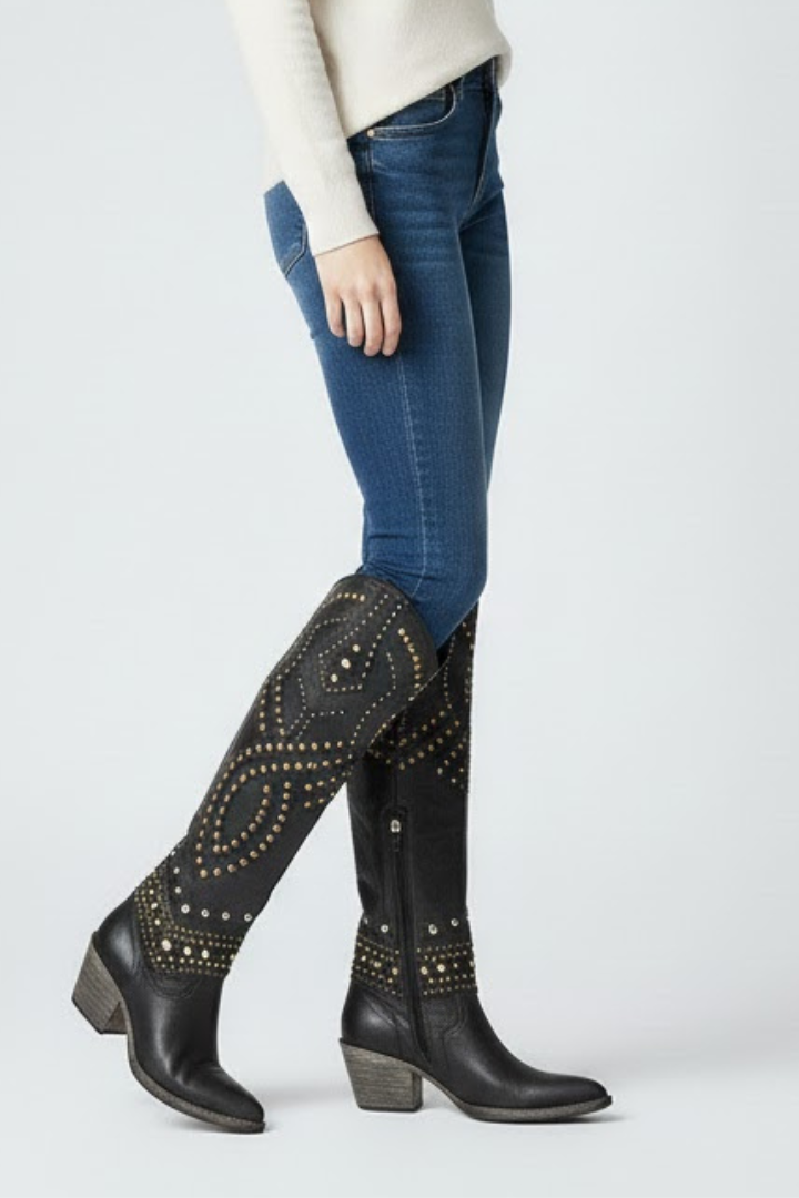 Black knee-high boots with decorative studs worn by a person on a white background