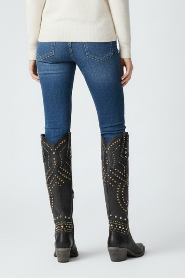 Person wearing blue jeans and black studded knee-high boots on a white background