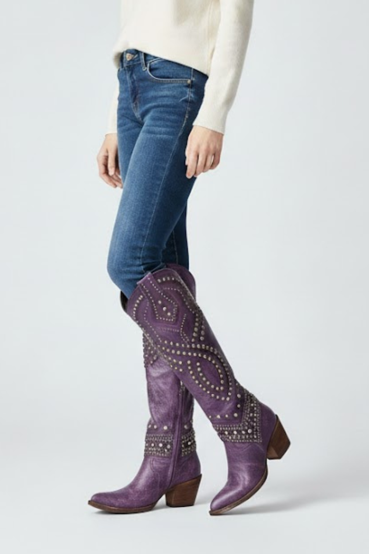 Person wearing blue jeans and purple studded boots on a white background