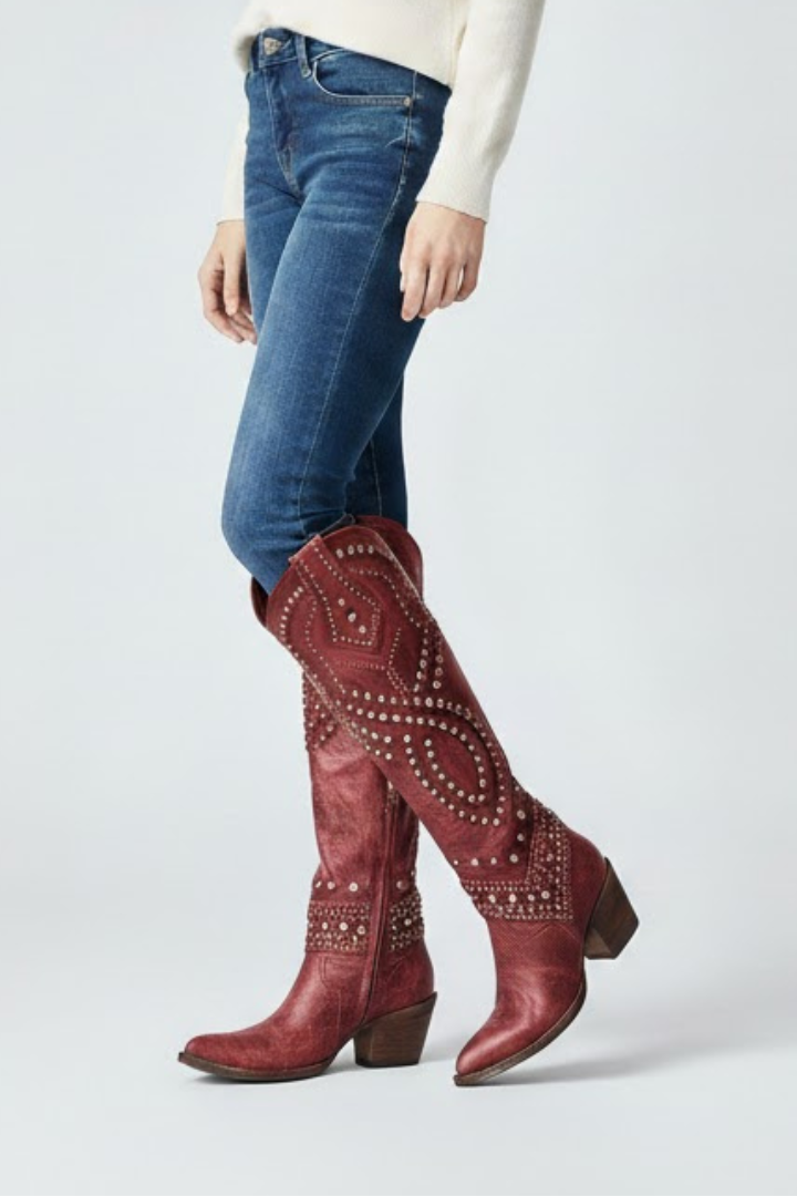 Red studded knee-high boots worn with blue jeans on a white background