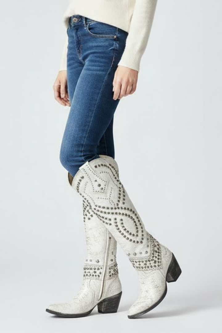 Person wearing blue jeans and white patterned knee-high boots on a light gray background