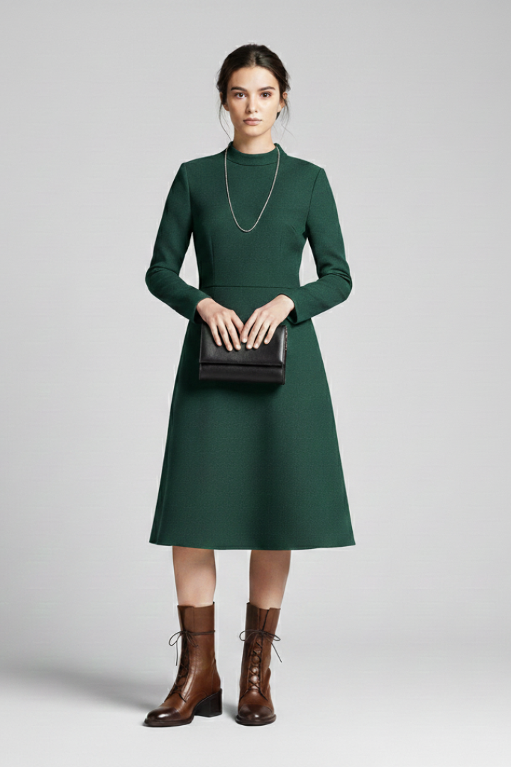 Woman wearing a green dress holding a black handbag on a gray background