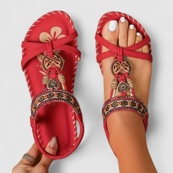 Red sandals with decorative straps and embellishments on a light gray background