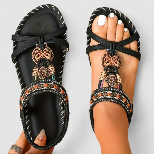 Decorative black sandals with intricate designs worn on a neutral background