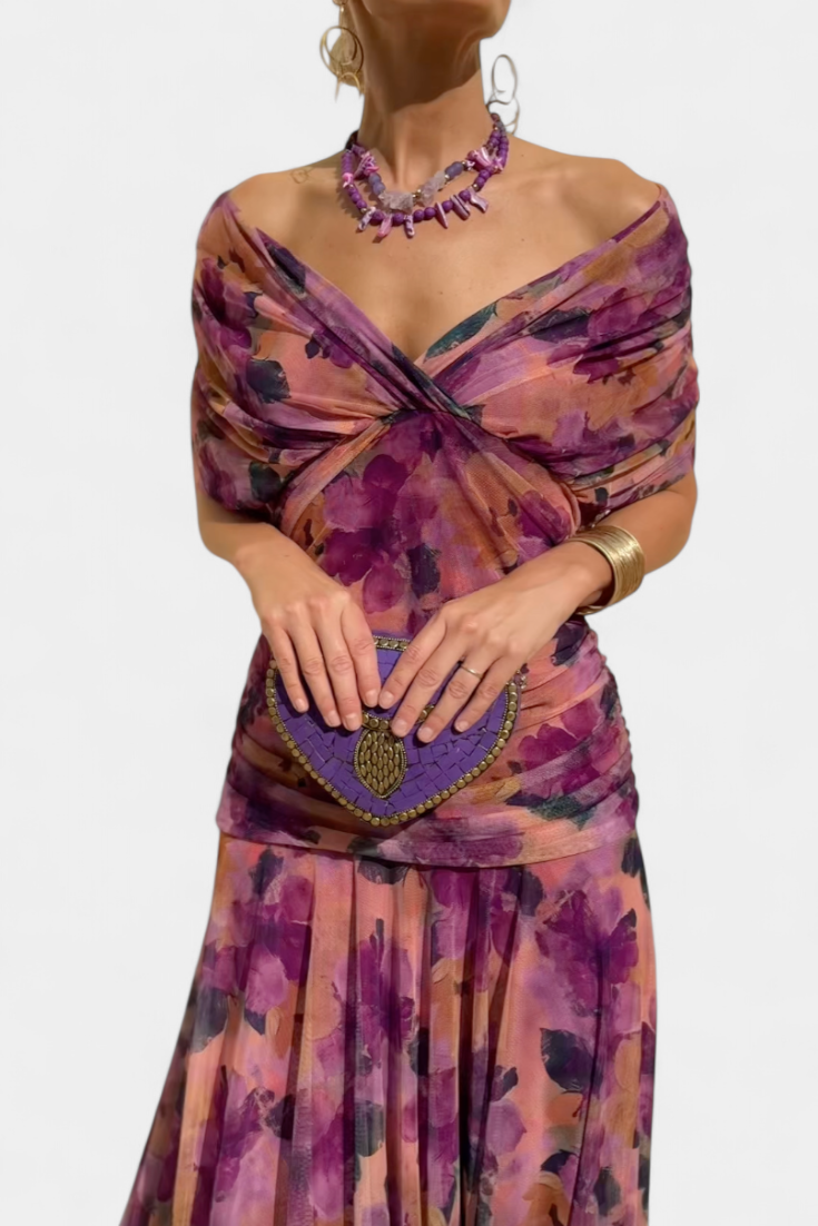 Woman wearing a floral dress with a purple clutch against a white background