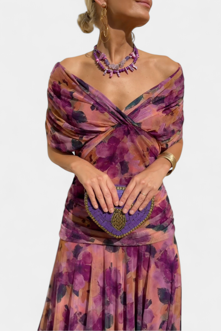 Woman wearing a colorful off-shoulder dress with a matching clutch and necklace on a white background