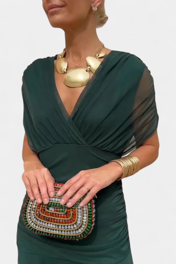 Woman wearing a green dress with gold jewelry and holding a beaded clutch.
