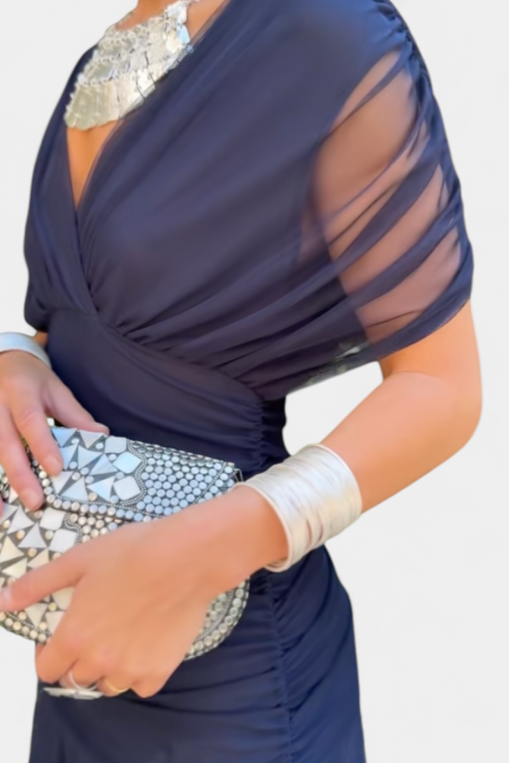 Navy blue dress with sheer sleeves and silver clutch held by a hand.