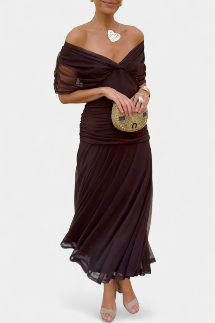 Woman wearing a brown off-shoulder dress holding a gold clutch on a white background