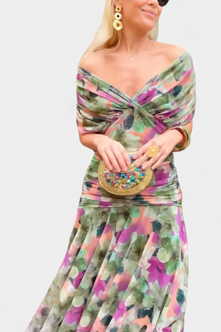 Woman wearing a colorful floral dress holding a gold clutch against a white background