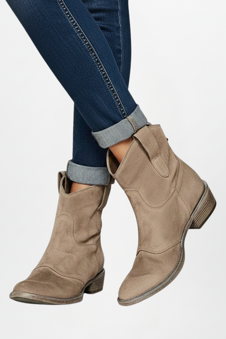 Beige ankle boots worn with rolled-up jeans on a light gray background