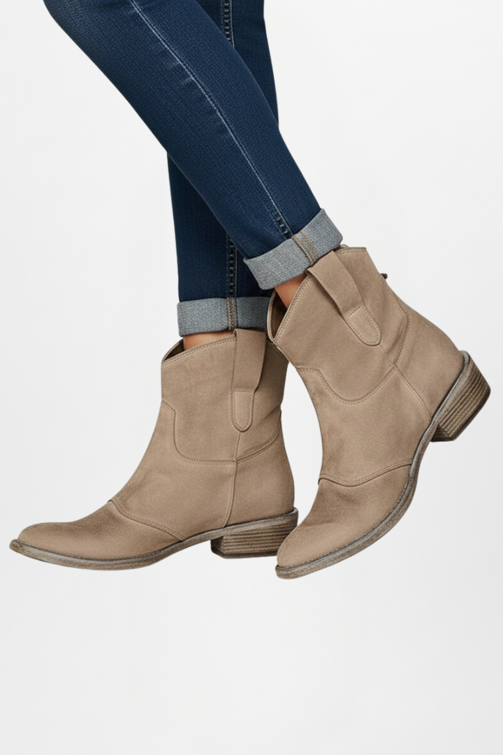Beige ankle boots worn with blue jeans on a white background