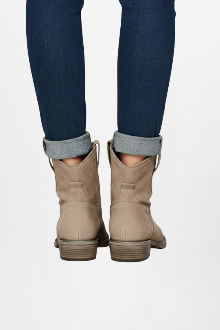 Tan cowboy boots worn with rolled-up jeans on a white background