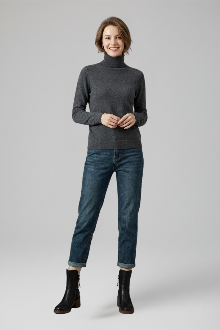 Woman wearing a gray turtleneck sweater, blue jeans, and black boots on a light gray background
