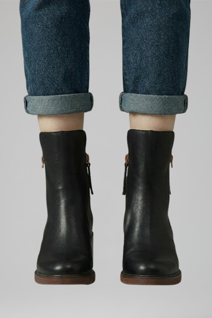 Black leather boots worn with rolled-up jeans on a gray background