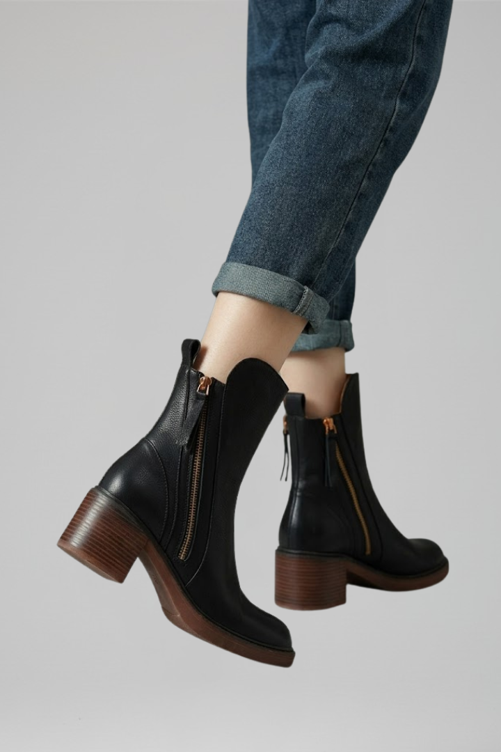 Black ankle boots with brown soles worn with rolled-up jeans on a gray background