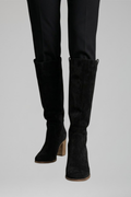 Black knee-high boots worn with black pants on a light gray background