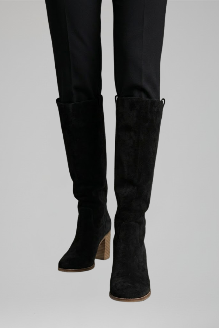 Black knee-high boots worn with black pants on a light gray background
