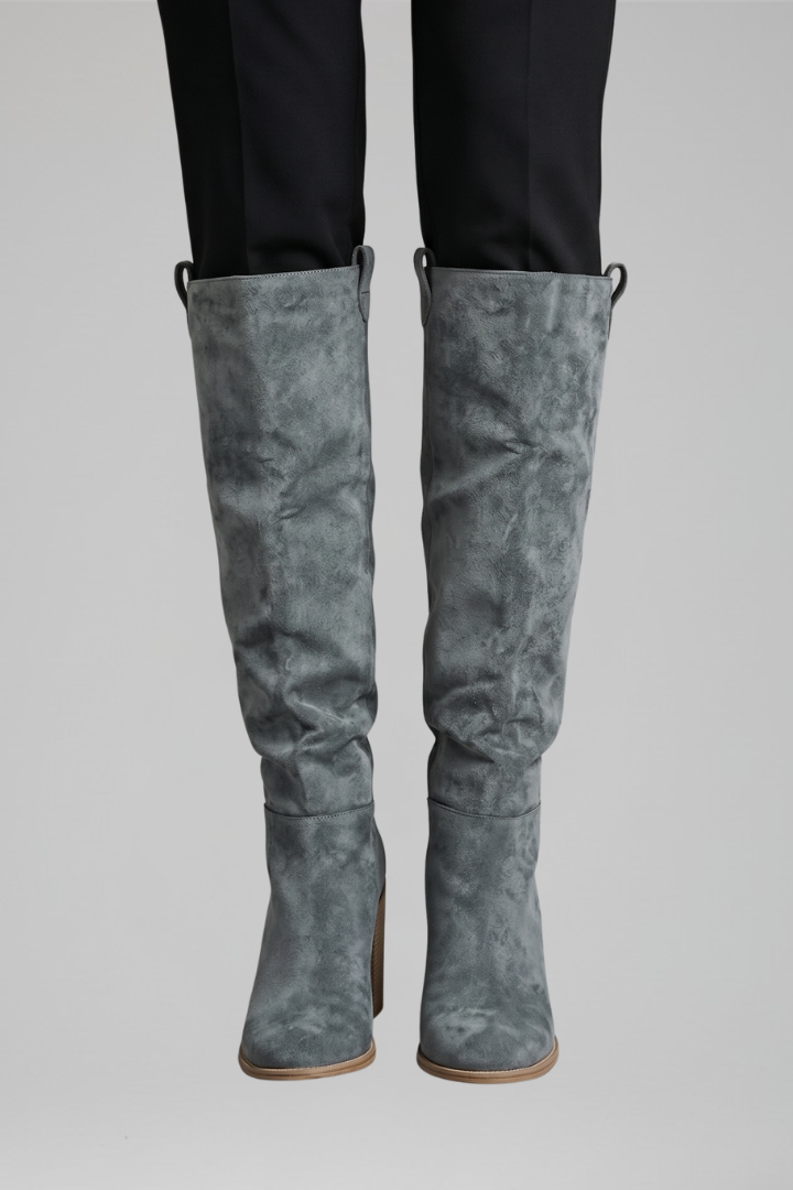 Gray suede knee-high boots worn with black pants on a gray background