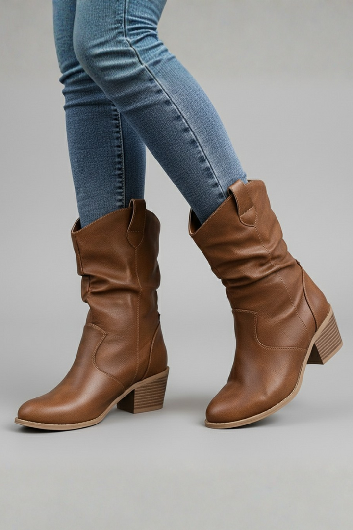 Brown knee-high boots worn with blue jeans on a gray background