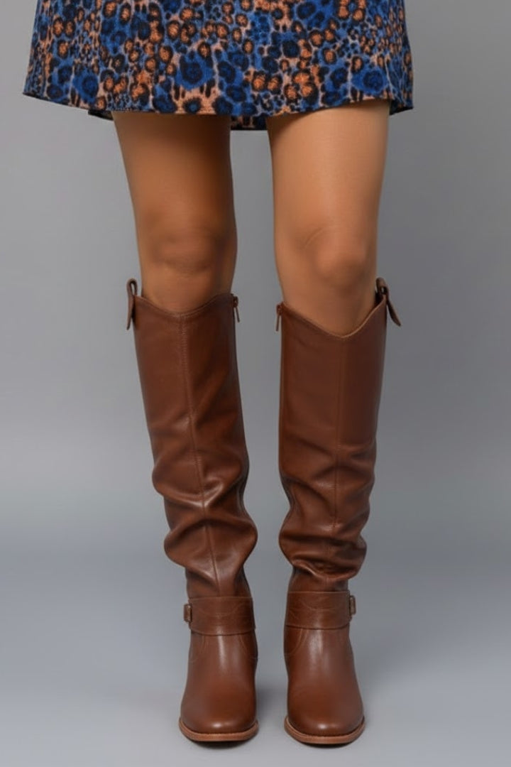Brown knee-high boots worn with a patterned dress on a gray background