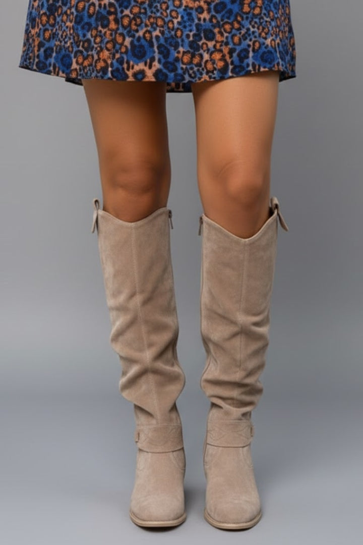Beige knee-high boots worn with a patterned dress on a gray background