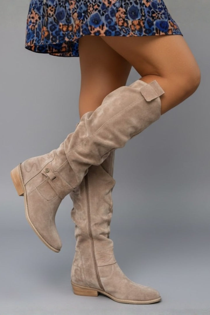 Beige knee-high boots worn with a blue floral dress on a gray background