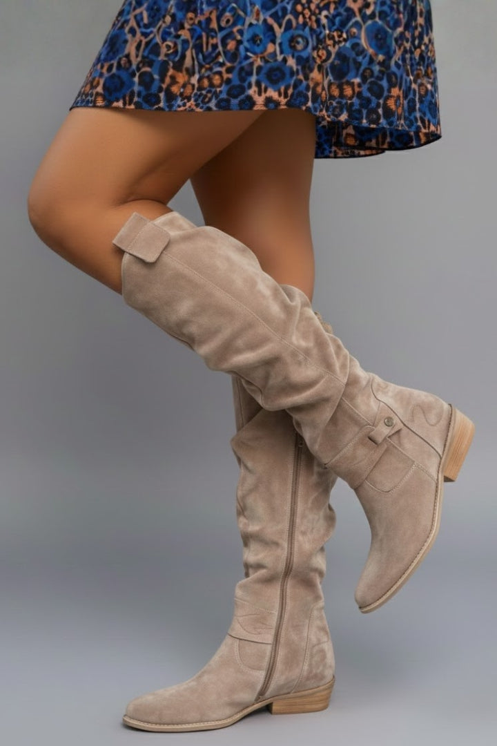 Beige knee-high boots worn with a blue floral dress on a gray background