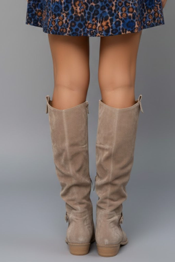 Beige knee-high boots worn with a patterned skirt on a gray background