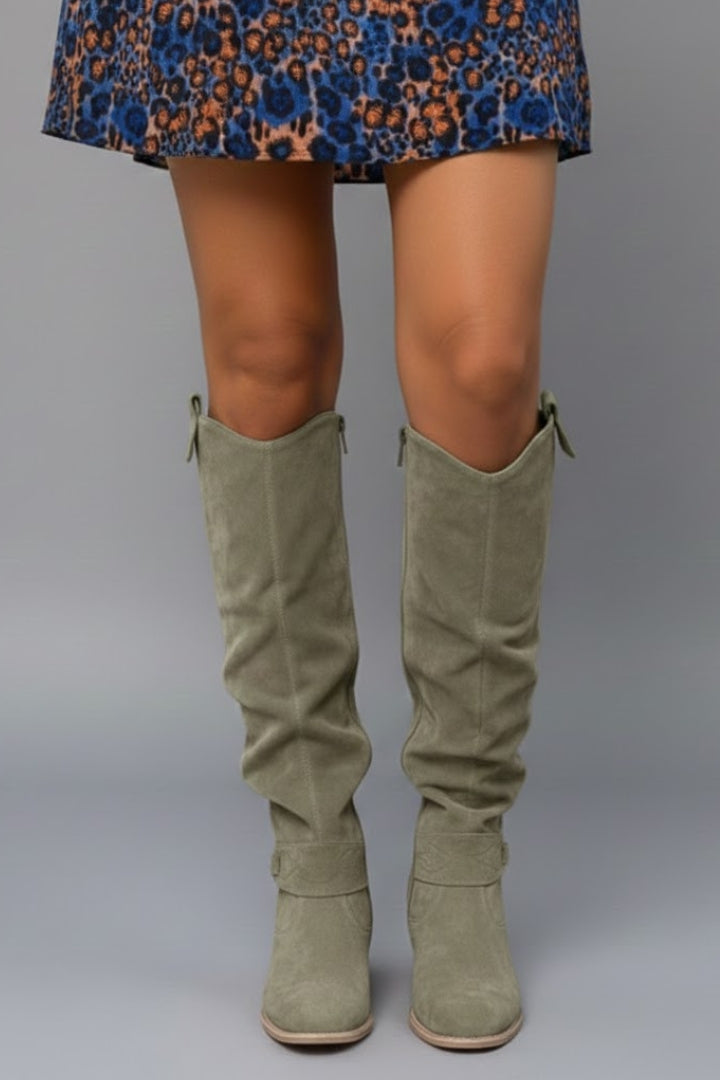 Green suede knee-high boots worn with a patterned dress on a gray background