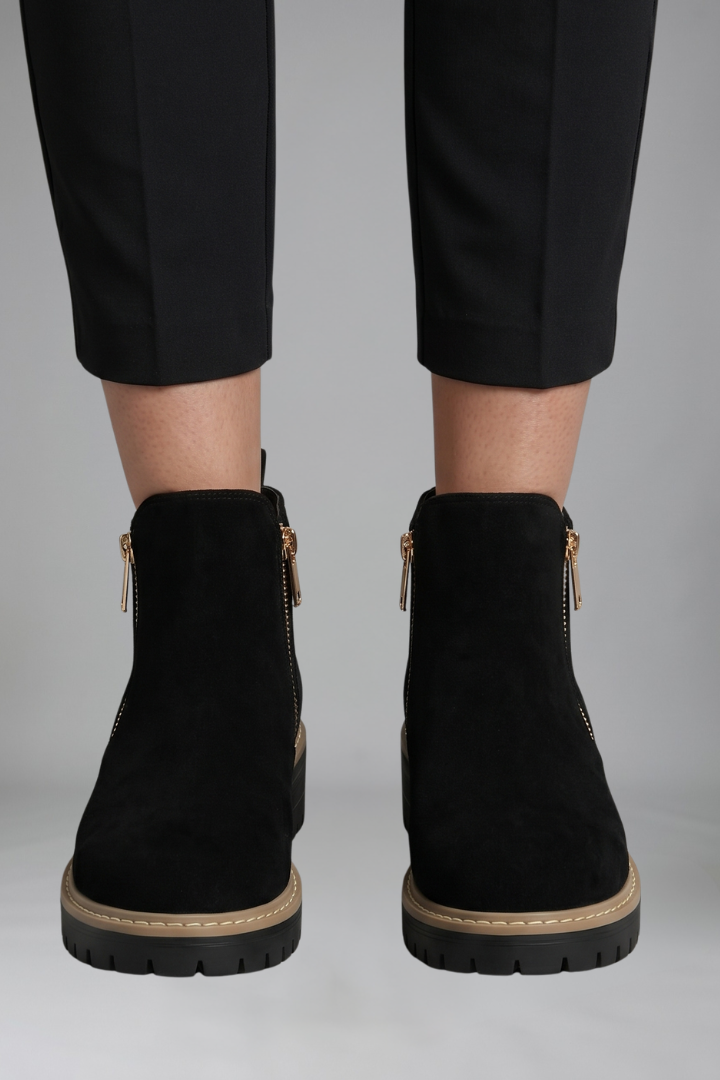 Black ankle boots with zippers worn with black pants on a gray background
