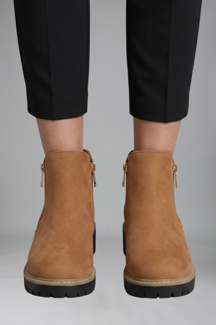 Brown ankle boots with zippers worn with black pants on a gray background