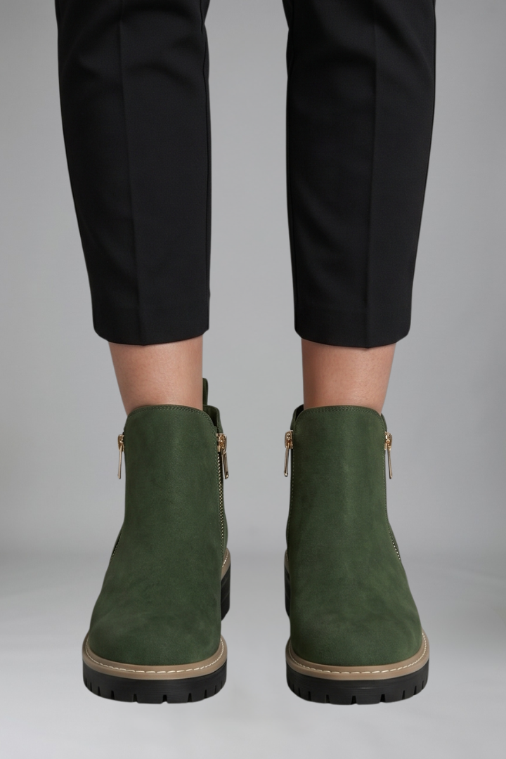Green suede ankle boots worn with black pants on a gray background