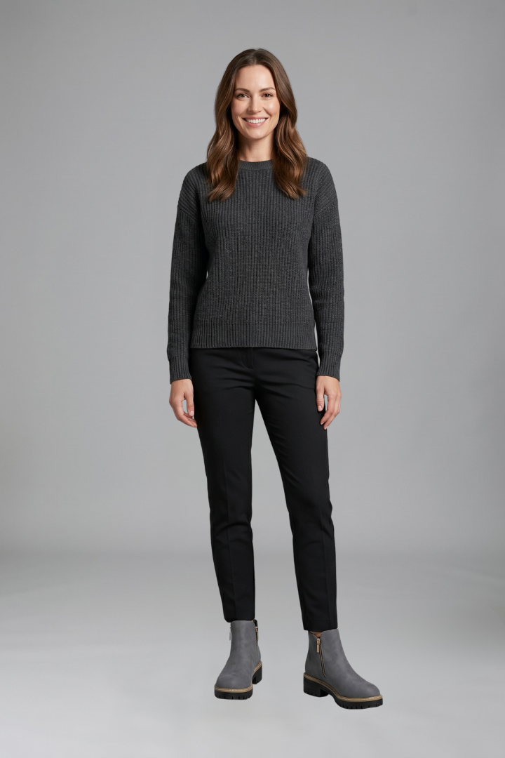 Woman wearing a gray sweater, black pants, and gray boots on a gray background
