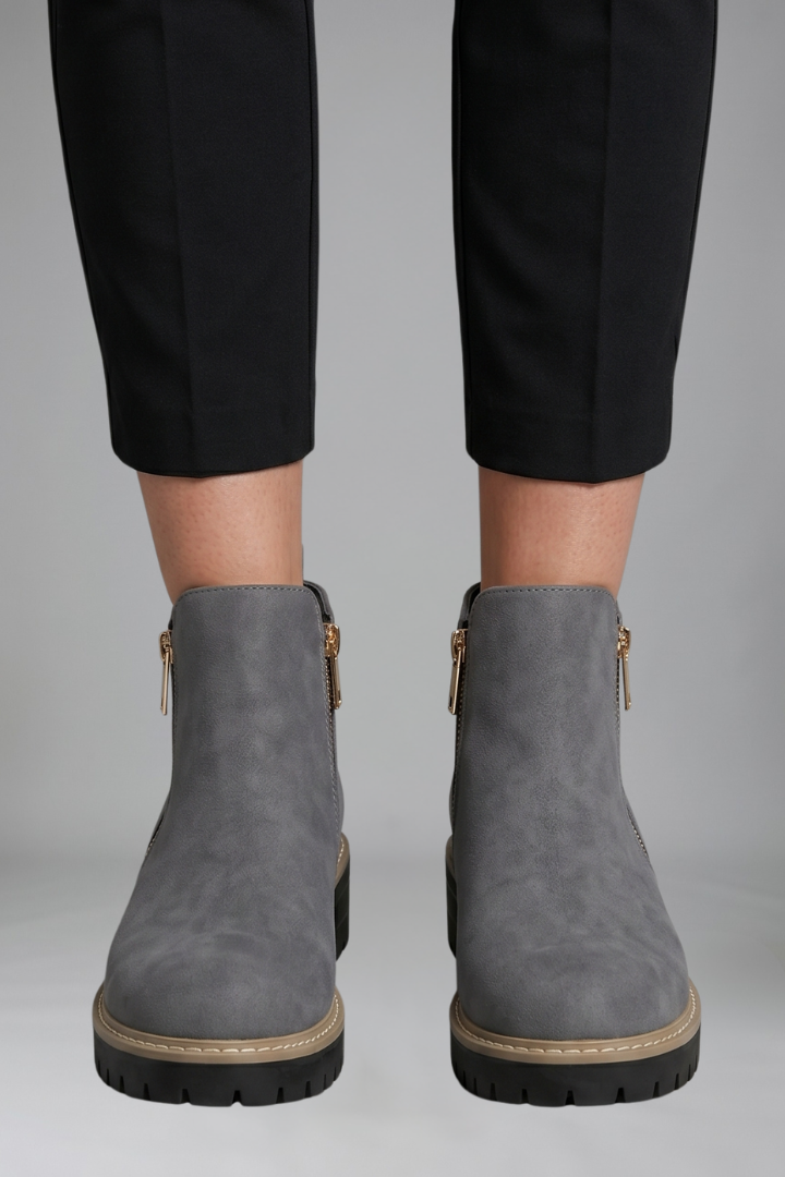 Gray ankle boots worn with black pants on a gray background