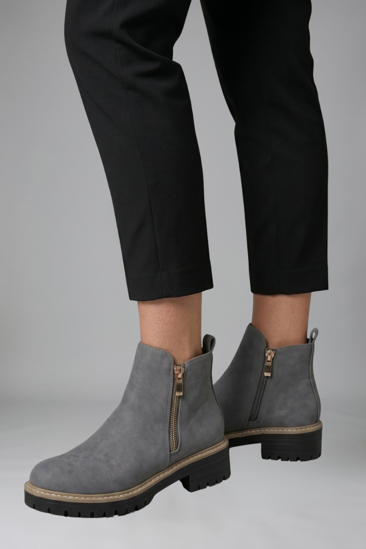 Gray ankle boots worn with black pants on a neutral background