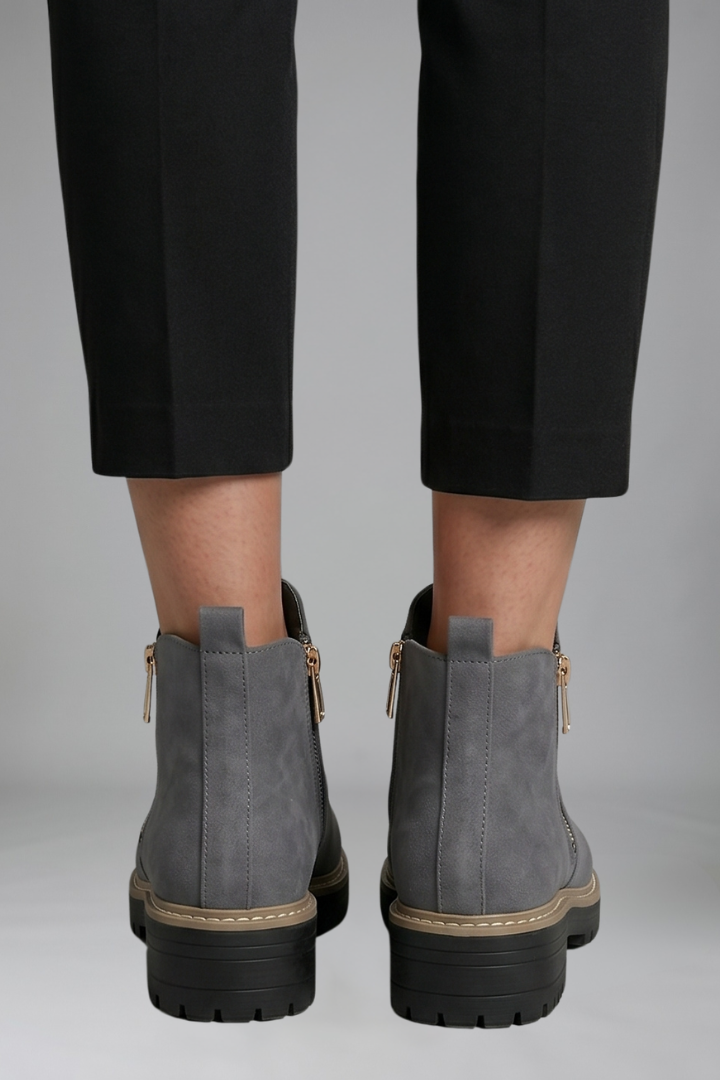 Gray ankle boots worn with black pants on a gray background