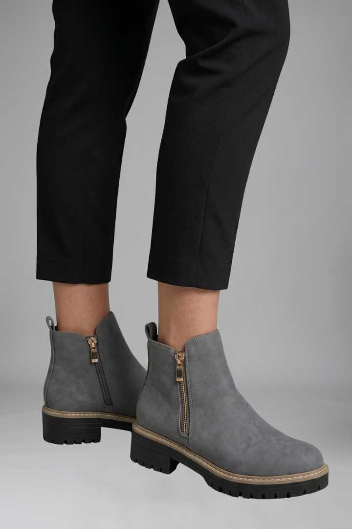 Gray ankle boots with zippers worn with black pants on a gray background