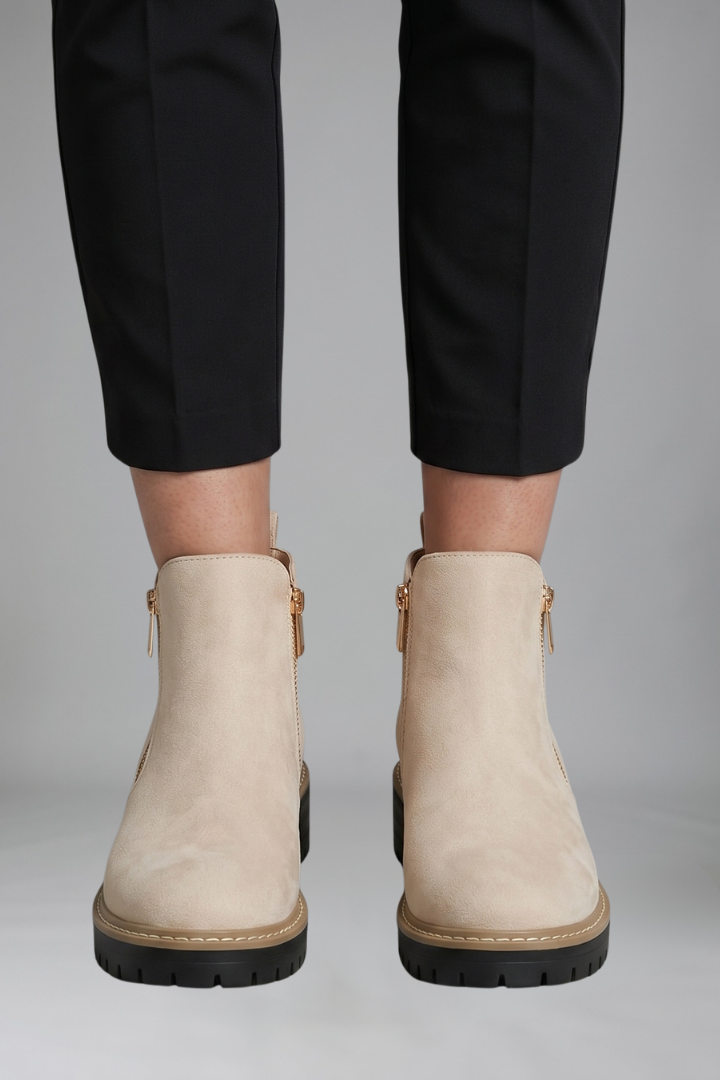 Beige ankle boots worn with black pants on a gray background