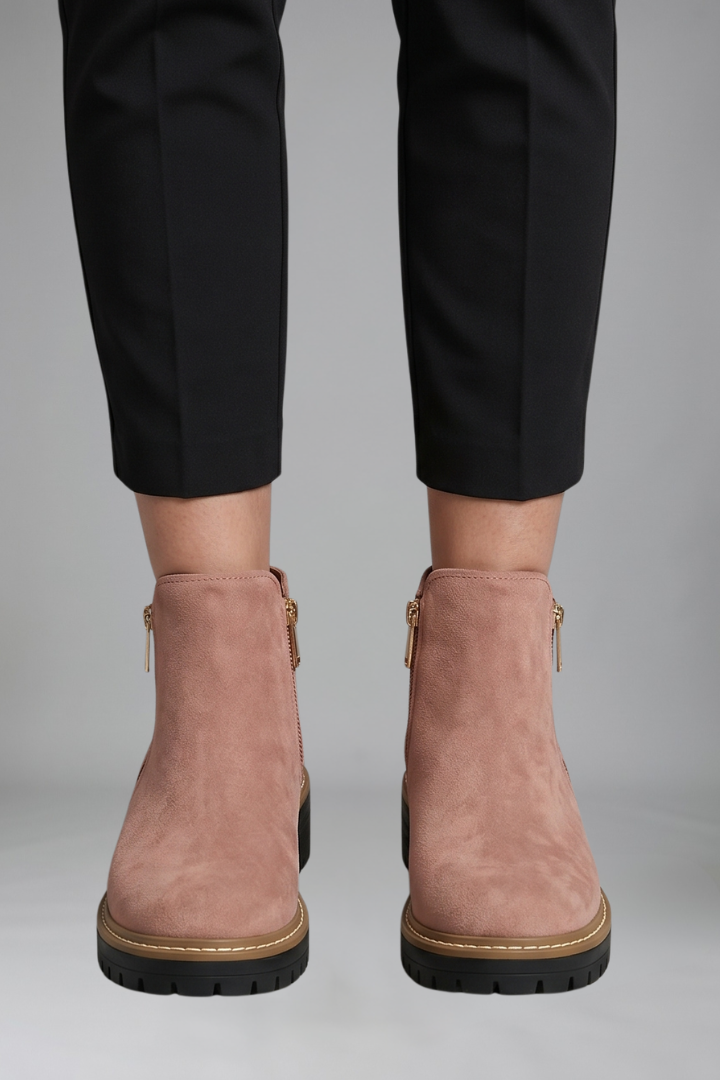 Pink ankle boots worn with black pants on a gray background