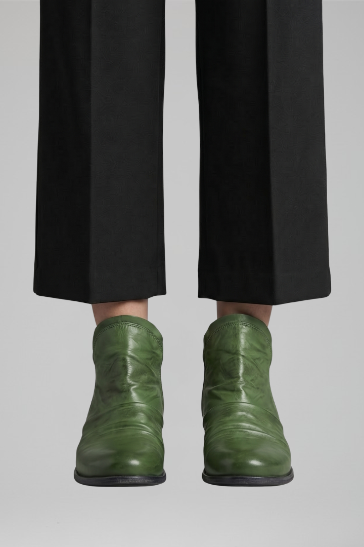 Green leather boots worn with black pants on a light gray background
