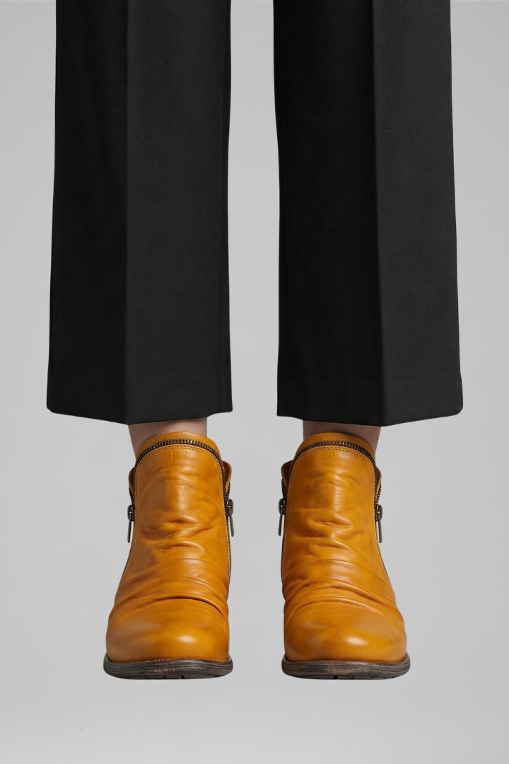 Person wearing brown leather boots and black pants on a light gray background