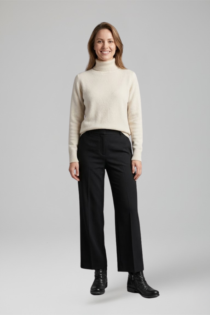 Woman wearing a cream sweater and black pants on a gray background