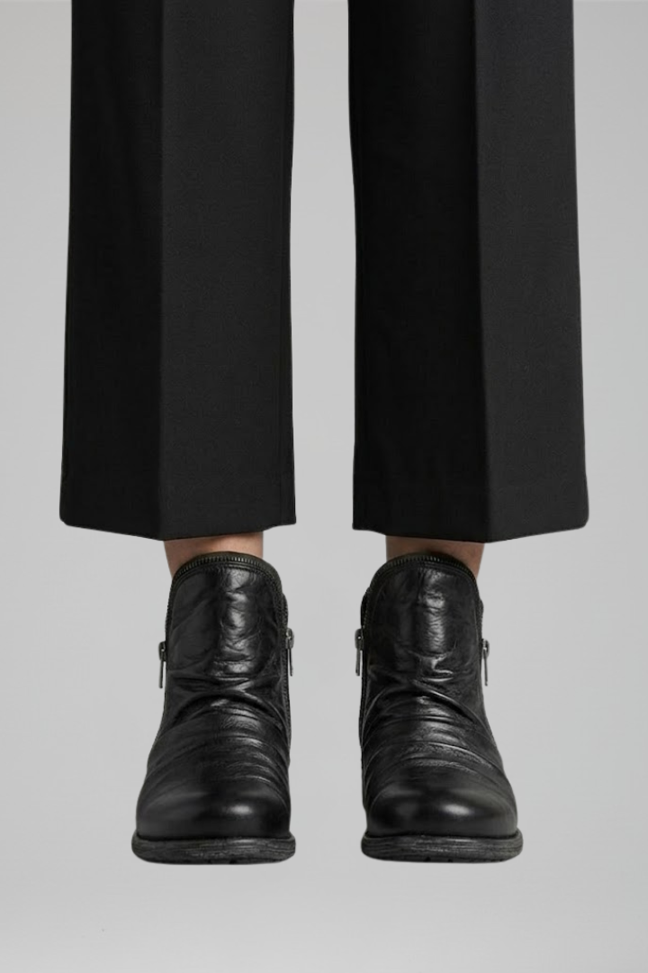 Black leather boots worn with black pants on a light gray background